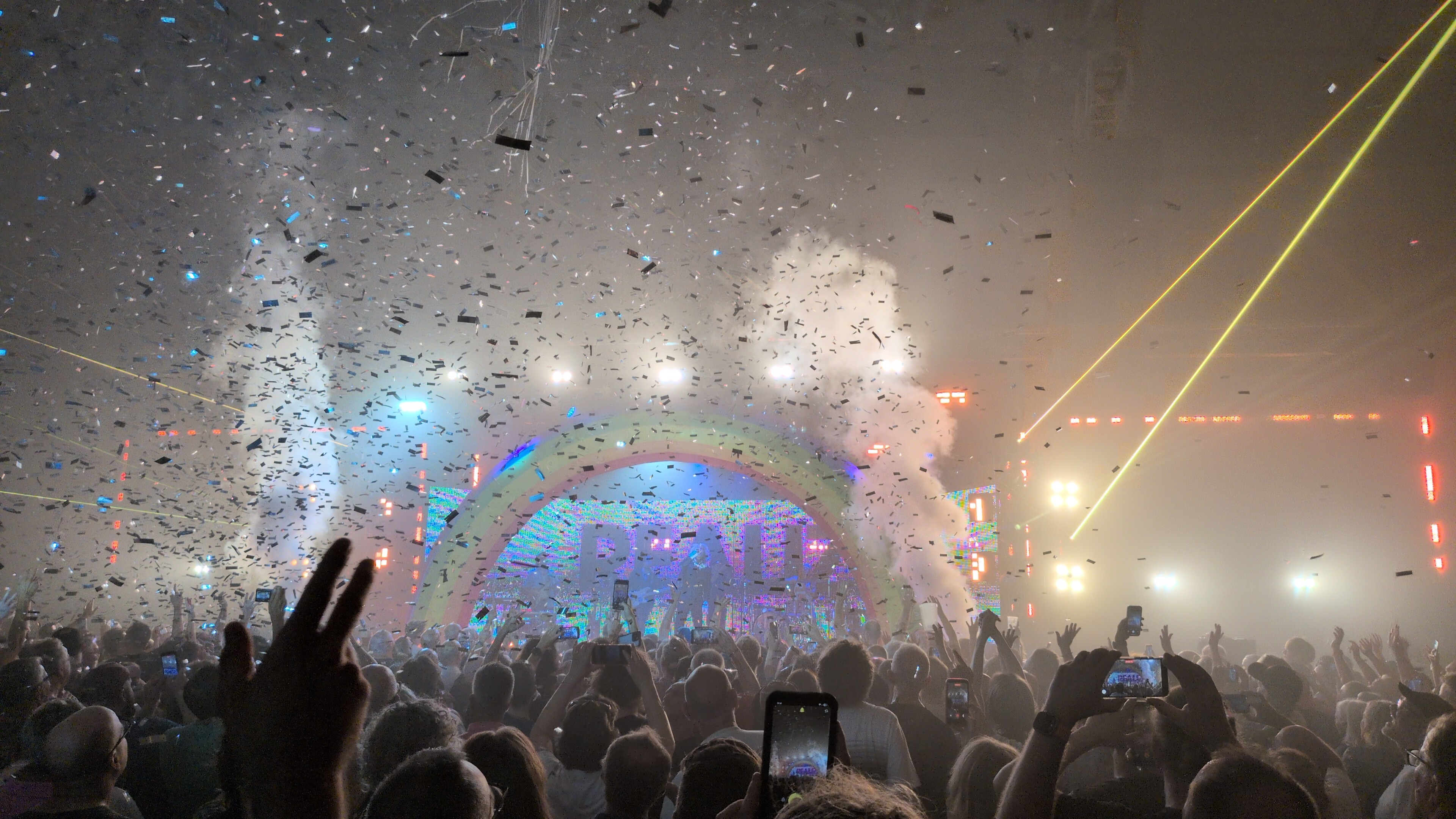 Photo at a gig.  A large inflatable rainbow frames the stage.  Smoke machines blast as confetti falls from the ceiling.
